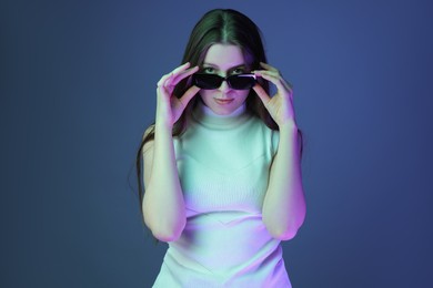 Portrait of beautiful young woman with sunglasses on color background with neon lights