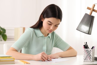 Photo of Teenage girl erasing mistake in her notebook at white desk indoors