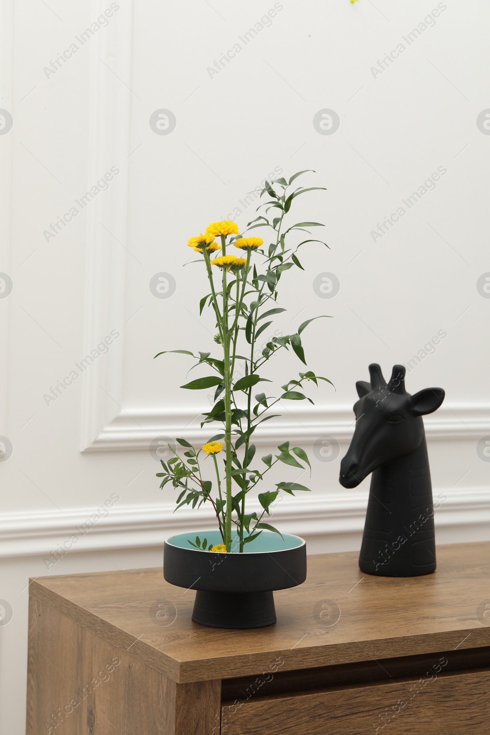 Photo of Stylish ikebana with beautiful yellow flowers, green branch and decor carrying cozy atmosphere at home