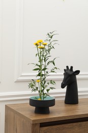 Stylish ikebana with beautiful yellow flowers, green branch and decor carrying cozy atmosphere at home