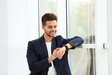Photo of Portrait of handsome young man looking at wristwatch near window
