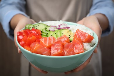 Woman holding delicious poke bowl with salmon and vegetables, closeup