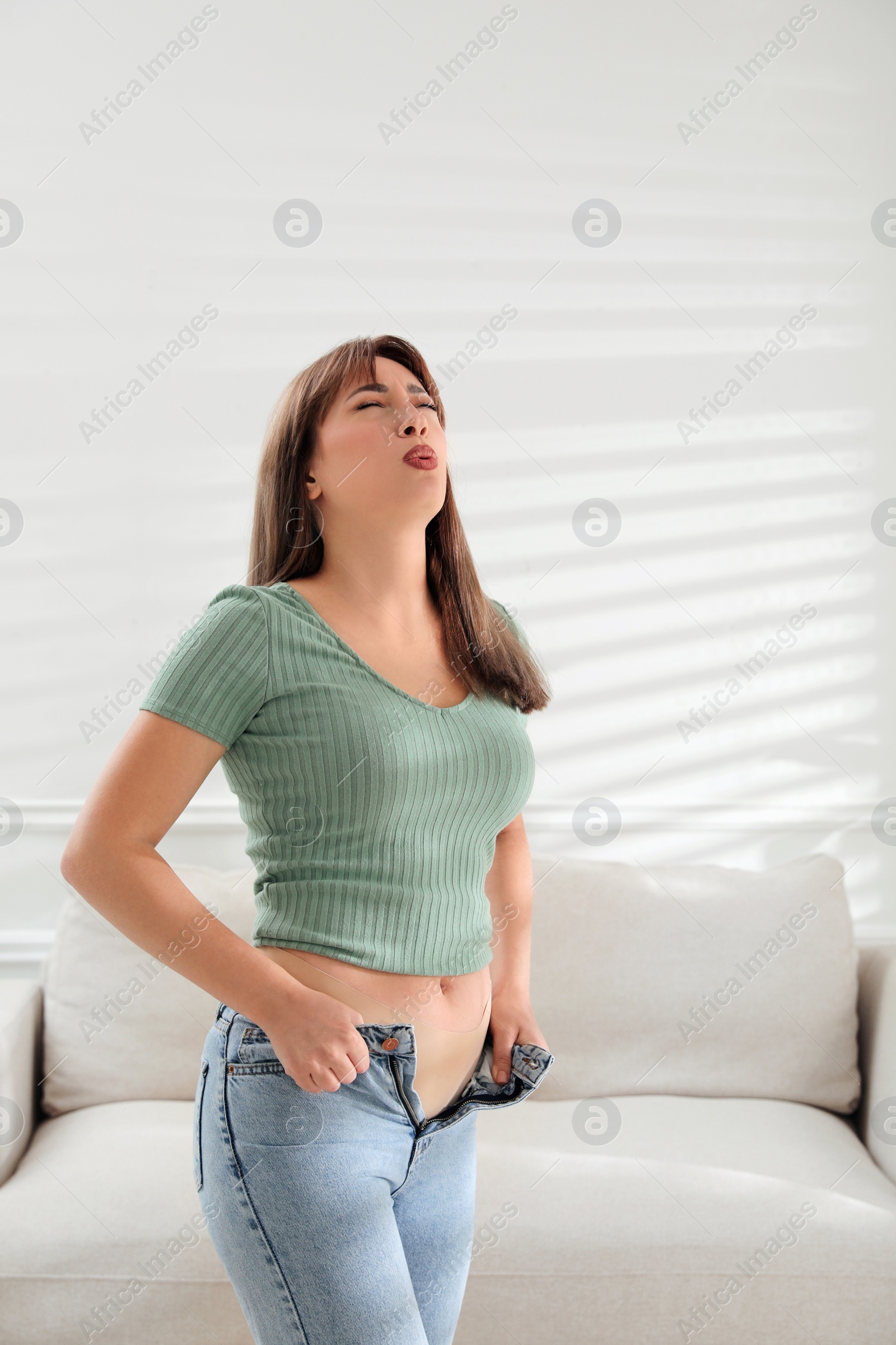 Photo of Young woman struggling to put on tight jeans at home