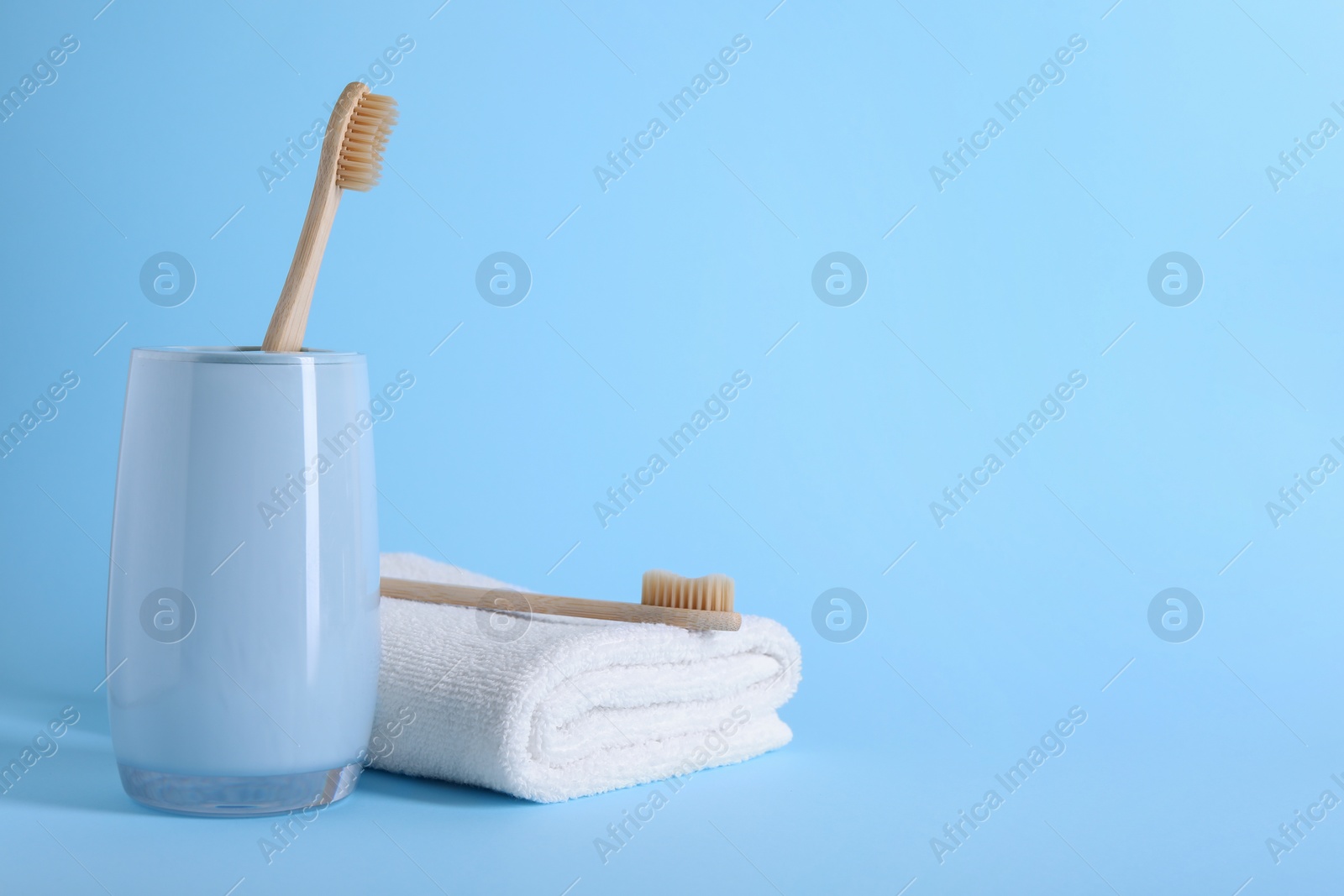 Photo of Bamboo toothbrushes and towel on light blue background, space for text