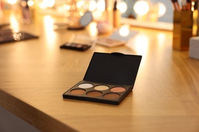 Photo of Eyeshadow palette and other makeup products on wooden dressing table