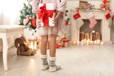 Cute little child hiding Christmas gift box behind back at home