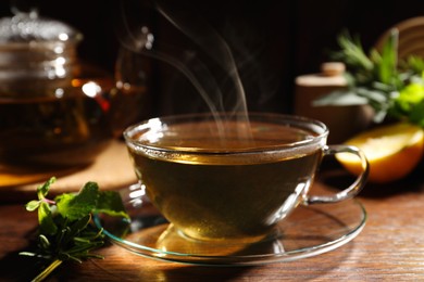 Photo of Cup of aromatic herbal tea, mint and rosemary on wooden table