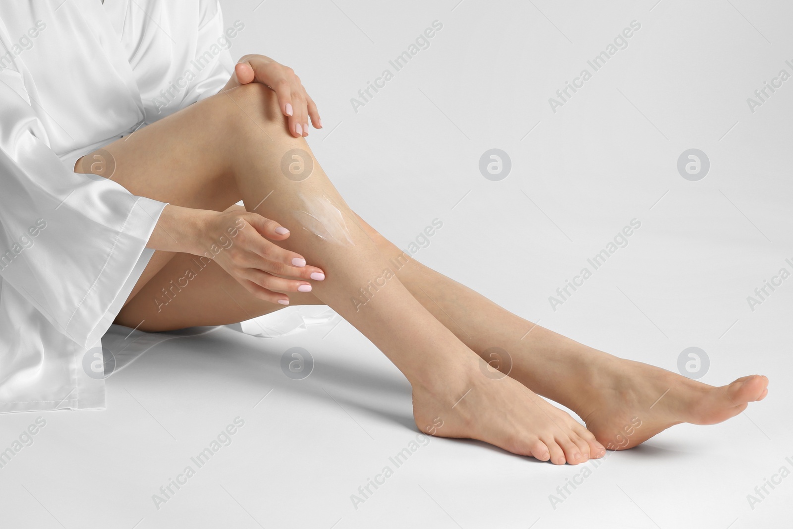 Photo of Woman applying body cream onto her smooth legs on white background, closeup