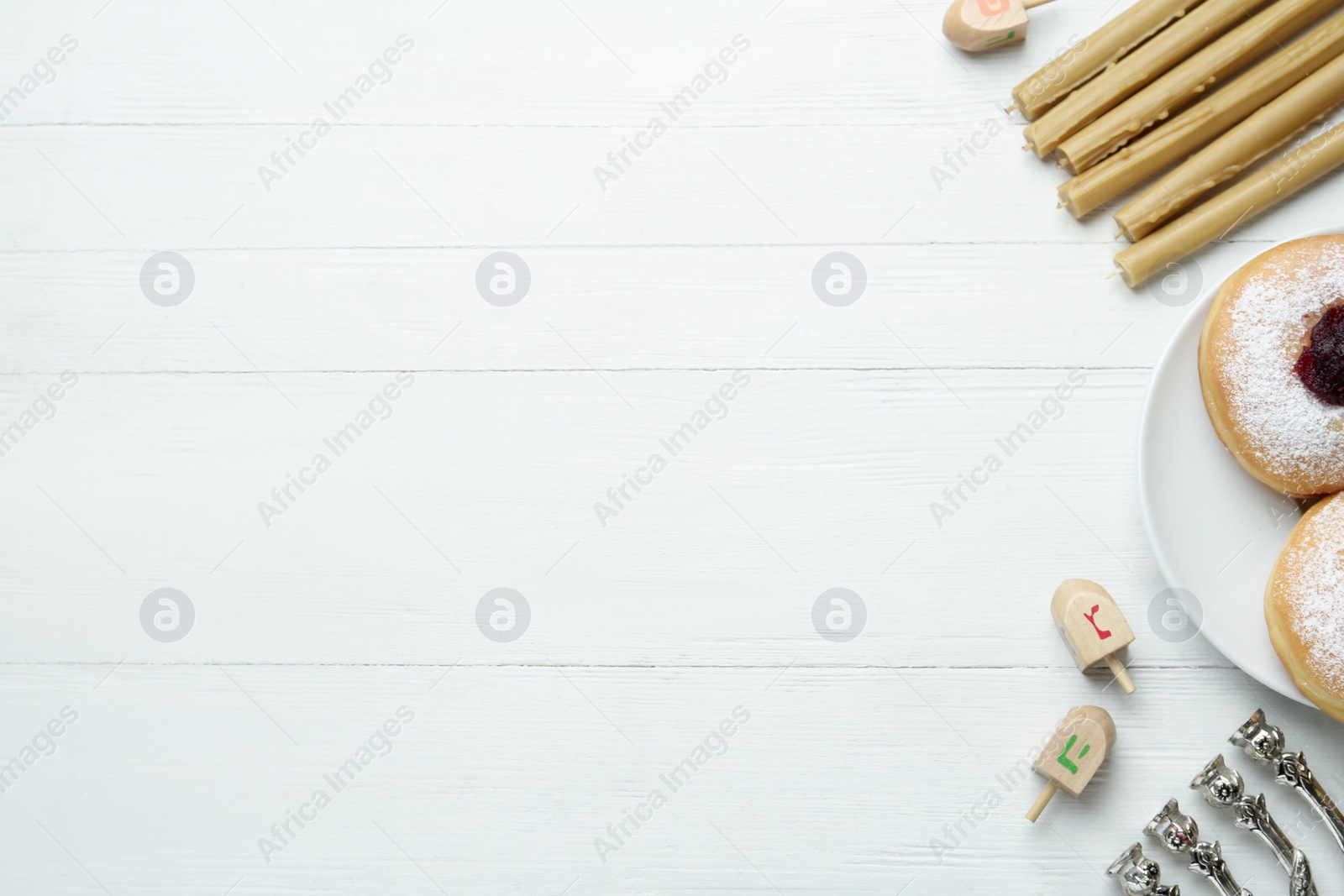 Photo of Flat lay composition with menorah, yellow candles, dreidels including He, Pe, Nun, Gimel letters and sufganiyot on white wooden table, space for text. Hanukkah symbols