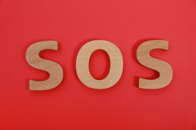Photo of Abbreviation SOS made of wooden letters on red background, top view