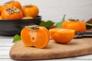 Photo of Whole and cut delicious ripe persimmons on white wooden table