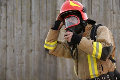 Firefighter in uniform wearing helmet and mask outdoors, space for text