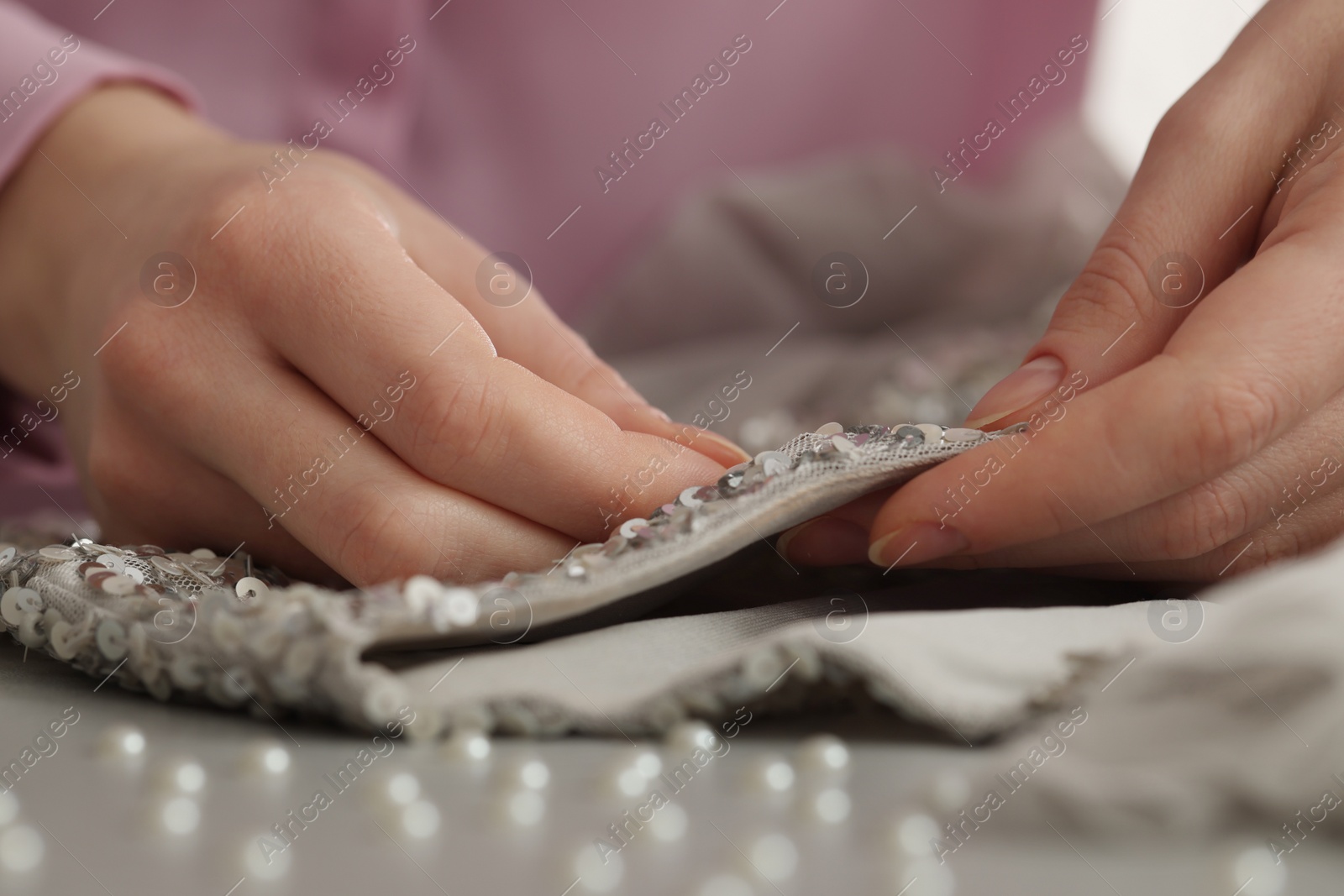 Photo of Dressmaker sewing party dress from silver fabric with paillettes at table in atelier, closeup