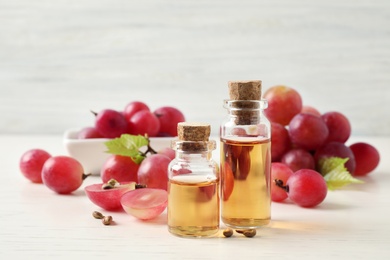 Photo of Organic red grapes, seeds and bottles of natural essential oil on white wooden table