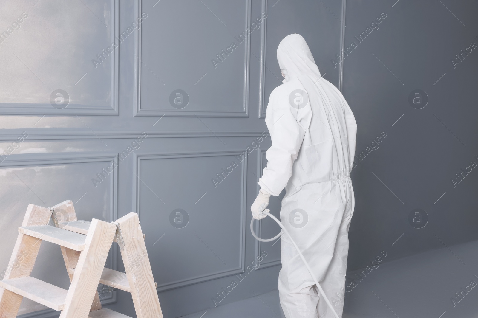 Photo of Decorator dyeing wall in grey color with spray paint indoors, back view