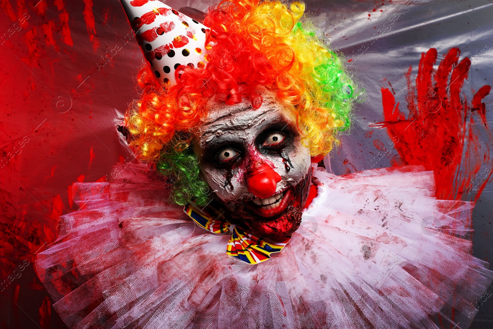 Photo of Terrifying clown near bloodstained plastic film. Halloween party costume