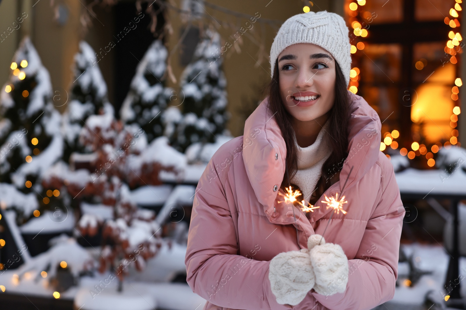 Photo of Portrait of smiling woman with burning sparkles on snowy city street. Space for text