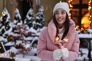 Portrait of smiling woman with burning sparkles on snowy city street. Space for text