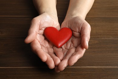 Photo of Elderly woman holding red heart in hands at wooden table, closeup