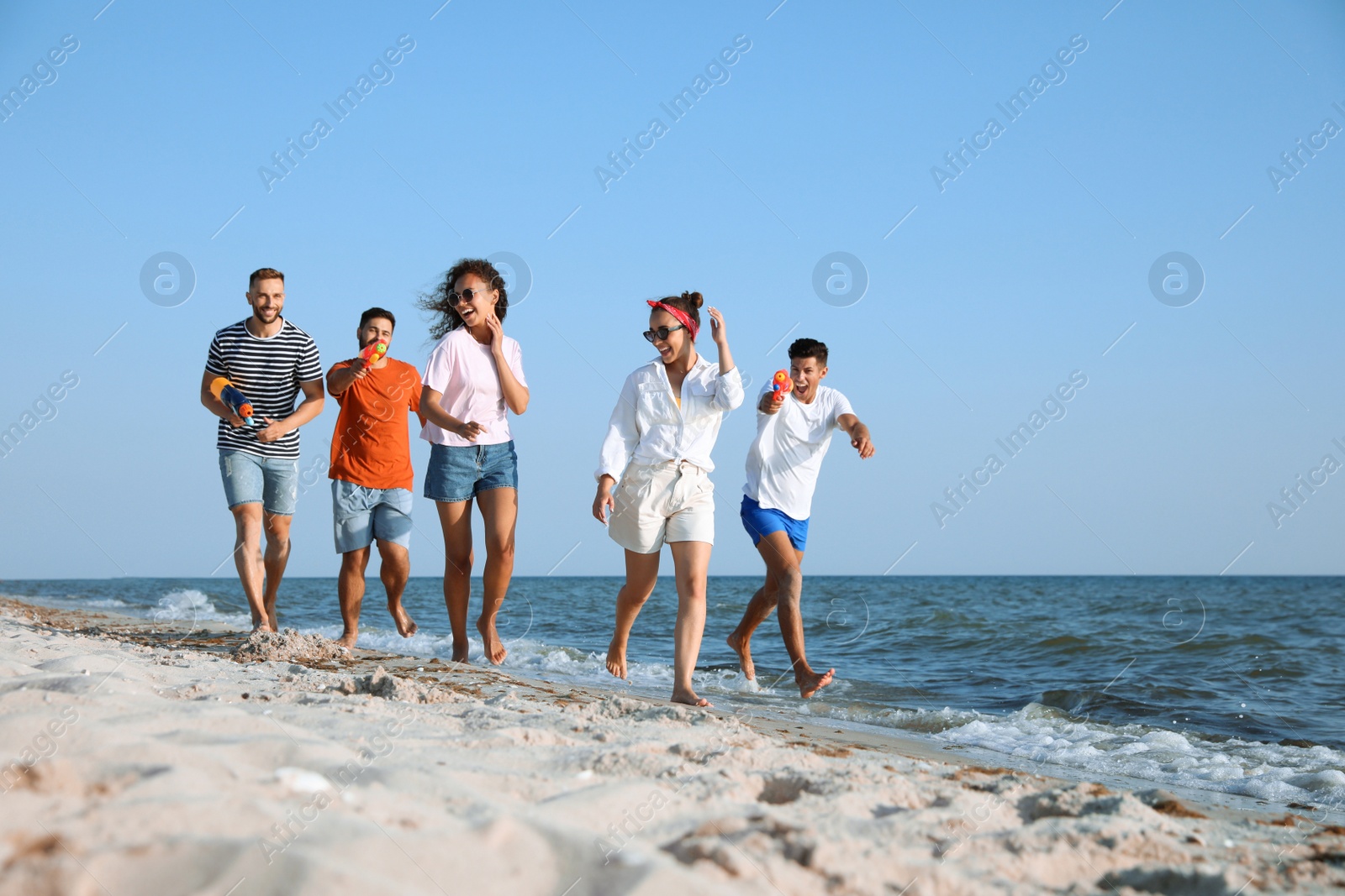 Photo of Group of friends with water guns having fun on beach