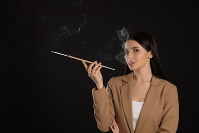 Woman using long cigarette holder for smoking on black background, space for text