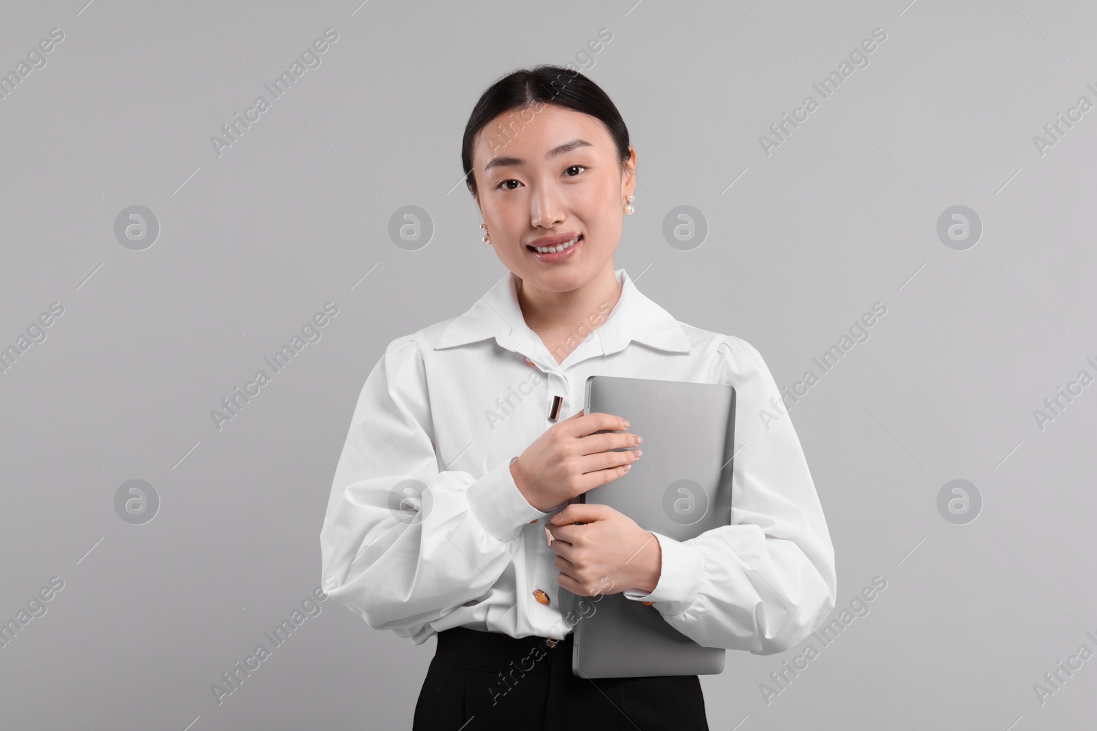 Photo of Portrait of smiling businesswoman with laptop on grey background