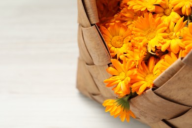 Photo of Beautiful calendula flowers in wicker bag on white table, closeup. Space for text