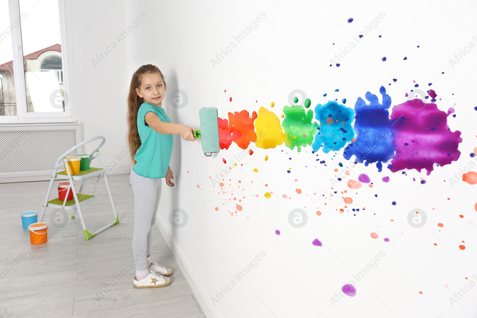 Image of Little girl drawing rainbow on white wall indoors