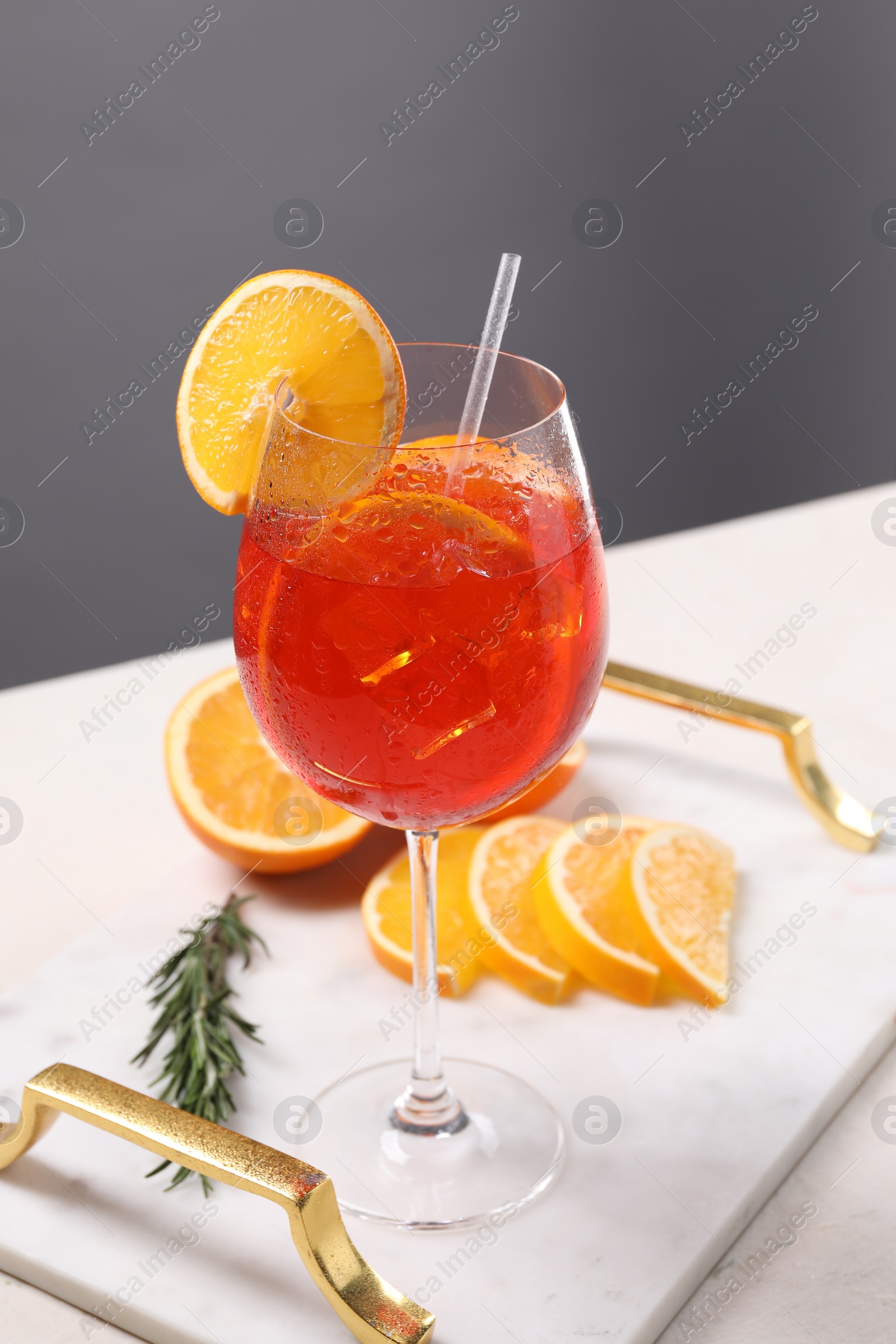 Photo of Glass of tasty Aperol spritz cocktail with orange slices and rosemary on white table against gray background