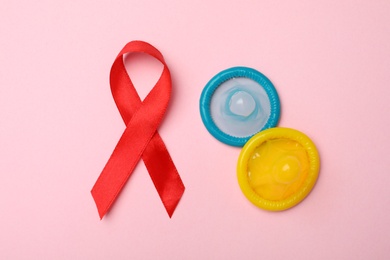 Flat lay composition with colorful condoms and red ribbon on pink background. LGBT concept