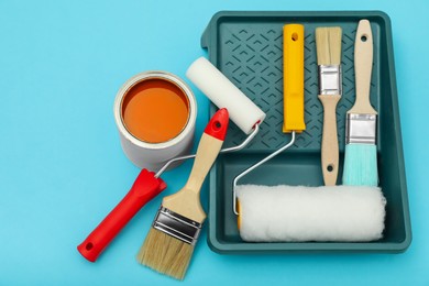 Photo of Can of orange paint, brushes, rollers and container on turquoise background, flat lay