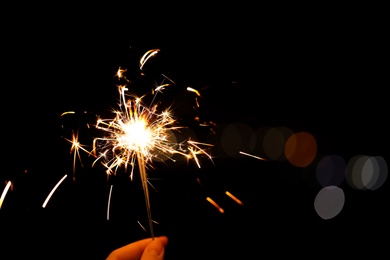 Photo of Woman holding bright burning sparklers against blurred lights, closeup. Space for text