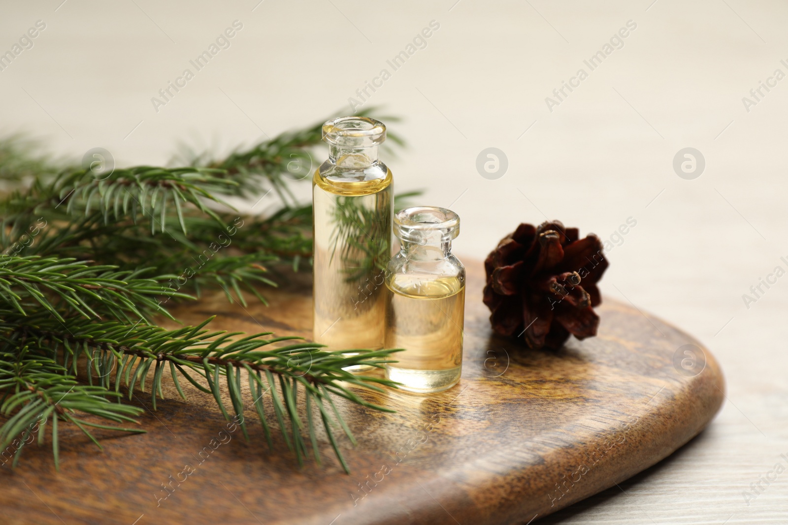 Photo of Pine essential oil, cone and branches on light wooden table