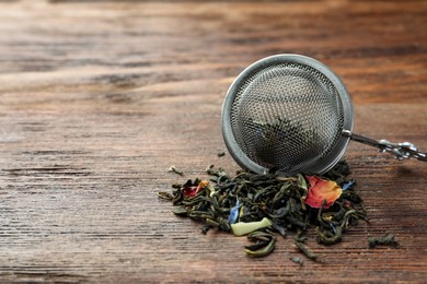 Photo of Snap infuser with dried herbal tea leaves on wooden table, closeup. Space for text