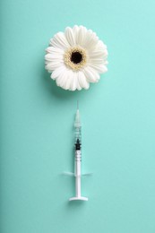 Photo of Cosmetology. Medical syringe and gerbera flower on turquoise background, flat lay