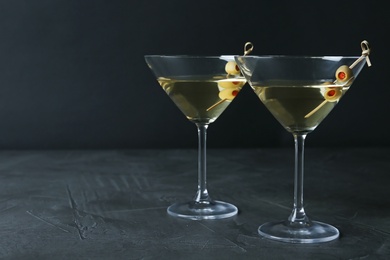 Photo of Glasses of Classic Dry Martini with olives on dark table against black background. Space for text