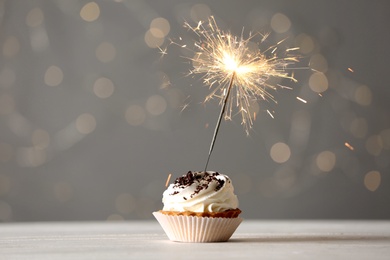 Photo of Delicious dessert with burning sparklers on white wooden table against blurred lights