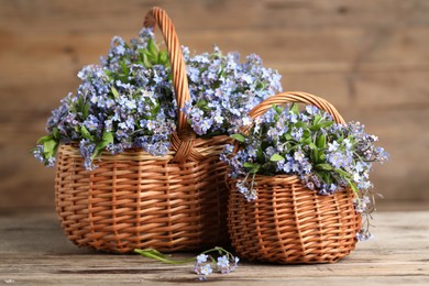 Photo of Beautiful forget-me-not flowers in wicker baskets on wooden table, closeup