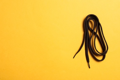 Brown shoelace on yellow background, top view. Space for text