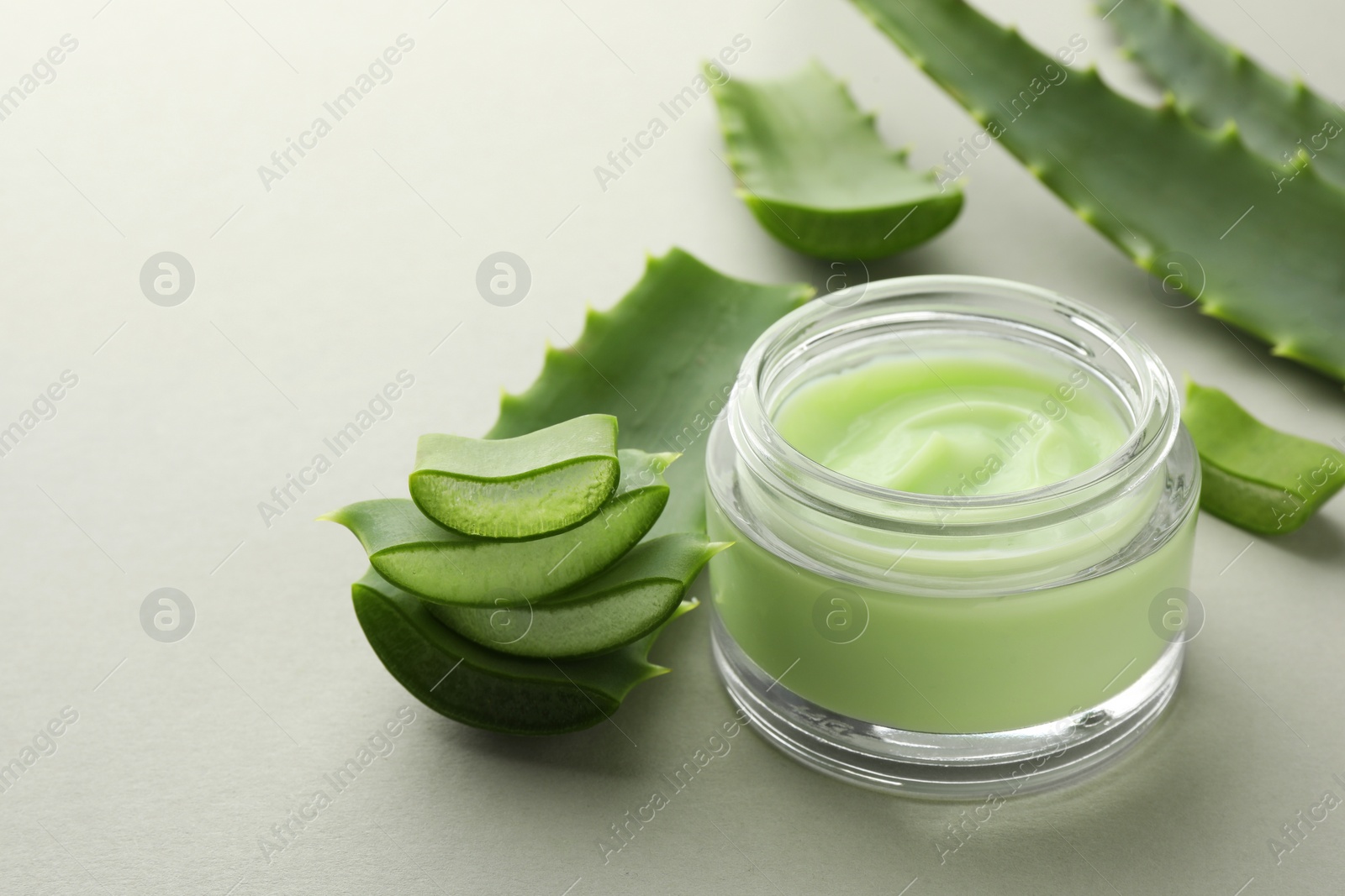 Photo of Jar with cream and cut aloe leaves on light grey background, closeup. Space for text