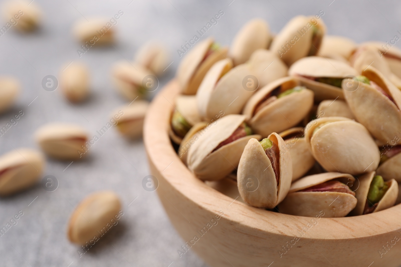 Photo of Delicious pistachios in bowl on grey textured table, closeup