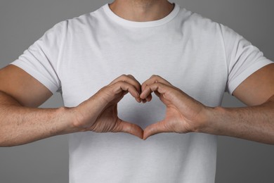 Photo of Man making heart with hands on grey background, closeup