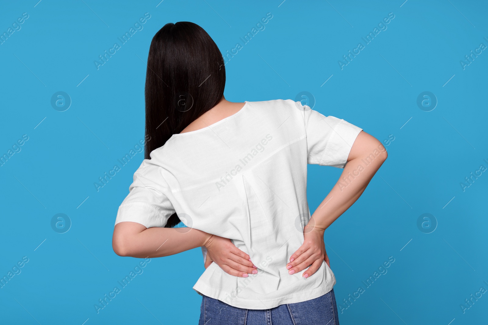 Photo of Young woman suffering from pain in back on light blue background. Arthritis symptoms