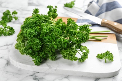 Fresh curly parsley, cutting board and knife on white marble table