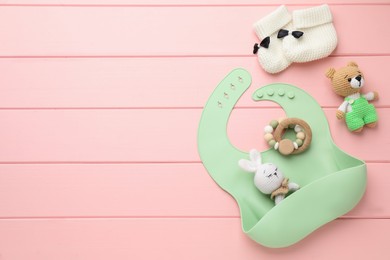 Photo of Flat lay composition with silicone baby bib, toys and accessories on pink wooden background. Space for text