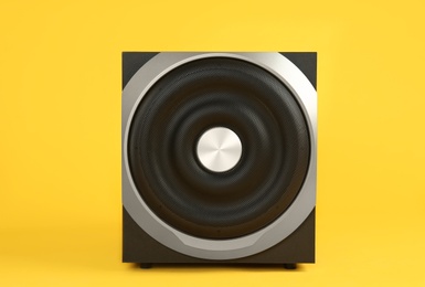 Photo of Modern subwoofer on yellow background. Powerful audio speaker