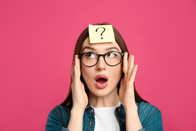Emotional woman with question mark sticker on forehead against pink background