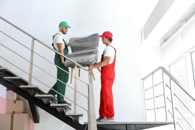 Photo of Male movers carrying armchair in new house