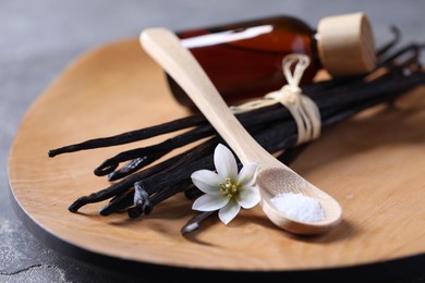 Photo of Spoon with sugar, flower, vanilla pods and bottle of essential oil on grey table, closeup