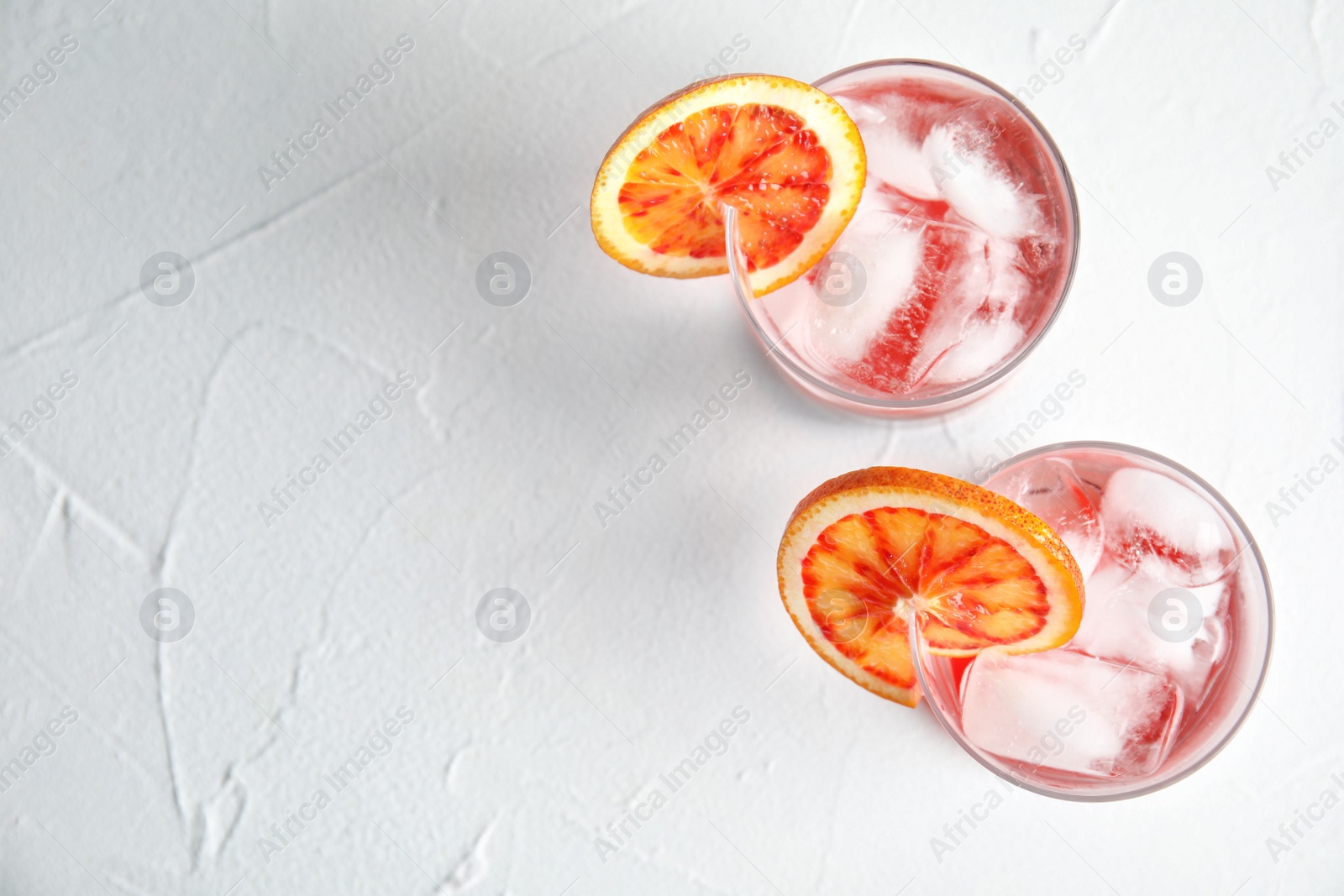 Photo of Glasses of drink with orange and ice cubes on white table, top view. Space for text